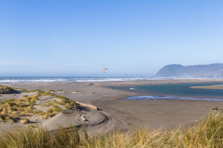 Man kite surfing in the mouth of the Pistol River with a rugged coast in the background characteristic of southern Oregonの写真素材