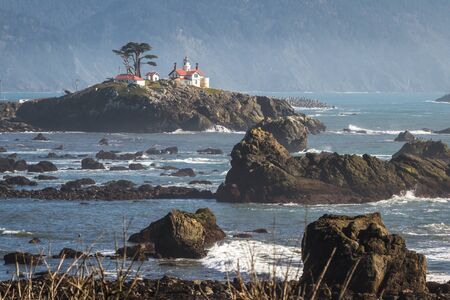 Tidal island just offshore Crescent City California home to one of the most visited structures in Del Norte County , Battery Point Lighthouse seen here at low tide with a bit of mist in the air against the dark mountains in the background.の写真素材