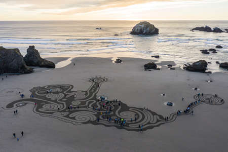 Bandon by the Sea, Oregon / USA - March 08 2020: People at sunset walking through a labyrinth on the beach of Face Rock State Park created by the team of Circles of the Sandのeditorial素材