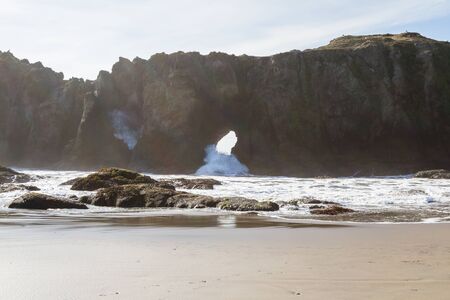 low tide revealing the size of this massive arch in a one of the sea stacks in Bandon Oregon with waves pushing thru creating a splashの写真素材