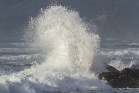 Rocky shoreline in Nesika Beach, Oregon late in the afternoon with the sun approaching the horizon and the waves crashing into the rocksの写真素材