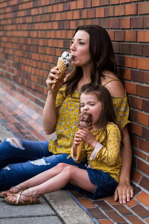 Mom and daughter eating ice cream outdoors with a brick wall in the background