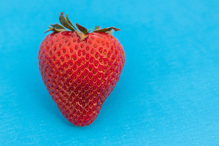 Single ripe red strawberry isolated on a blue background