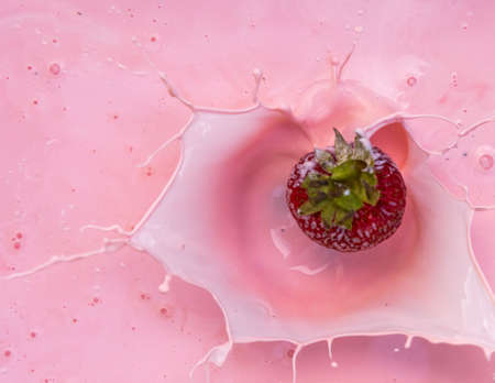 Action image of a strawberry splashing into a bowl of pink creamの写真素材