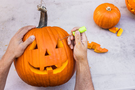 Hands holding and carving a smiling pumpkin outdoors with pieces on the tableの写真素材