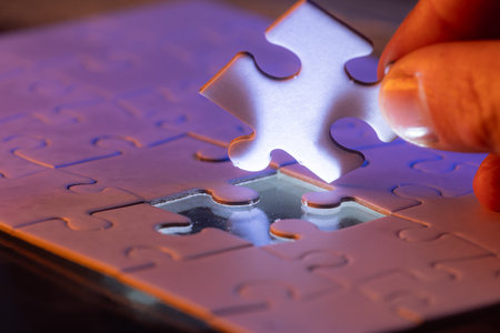 close up of a hand holding the missing puzzle piece with a glow showing where the piece goes and a bit of mist in the air.の写真素材