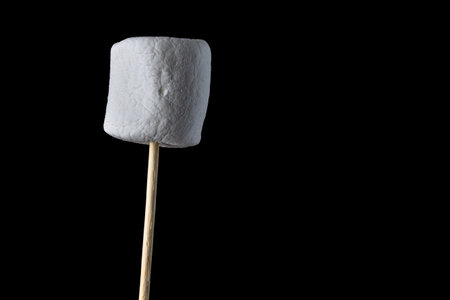 close up of a fresh marshmallow on a stick isolated on a black background.の写真素材
