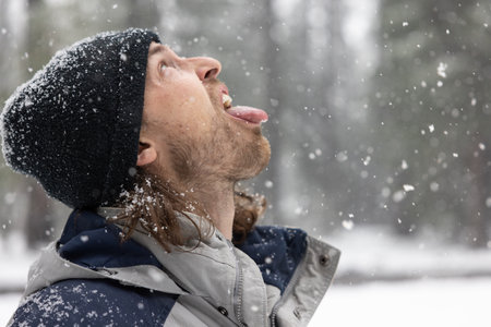 A man with a black hat and beard is making a funny face and sticking his tongue out in the snowの写真素材