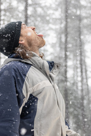 A man wearing a black hat and a blue jacket is standing in the snow with his mouth openの写真素材