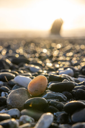 A small rock is sitting on a beach with a large rock in the background. The rock is surrounded by...