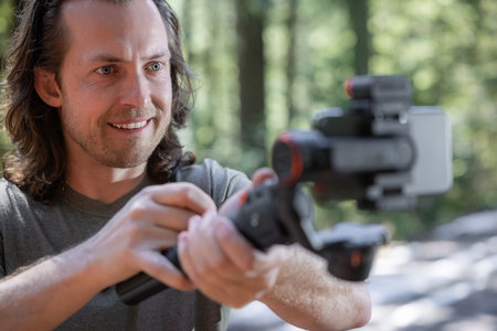 Content creator using. a phone gimbal to film in nature with a blurred forest in the background