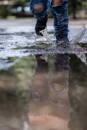 A person is walking in the rain with their feet in the water. The reflection of the person and their...
