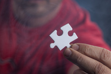 Concept for problem solving, a mans hand holding a blank puzzle piece with the man slightly out of focus in the background.の写真素材