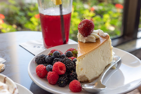 A slice of cheesecake with strawberries, blueberries and raspberries on top of a white plate. A...