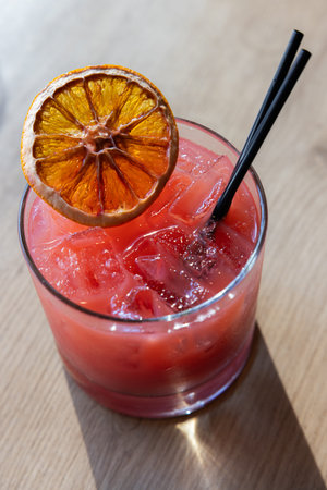 A glass of pink drink with a slice of orange on top. The drink is served in a short glass with a...