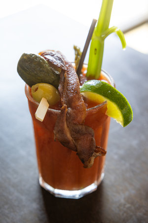 A glass of Bloody Mary with bacon and pickles on top. The drink is garnished with a lime wedge, olives, celery and a pickle spearの写真素材