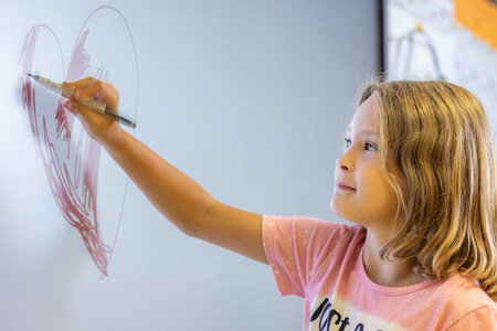 A girl is drawing on a digital white board with a marker. She is smiling and seems to be enjoying herselfの写真素材