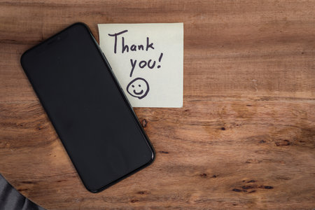 A cell phone with a smiley face sticker on it and a note that says "Thank You" on top of itの写真素材
