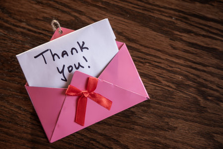 A pink envelope with a red ribbon and a note that says "Thank You!" on it. Concept of gratitude and appreciationの写真素材