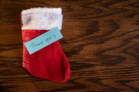 A blue note with the words Thank You written on it is placed on top of a red Santa Stalking.