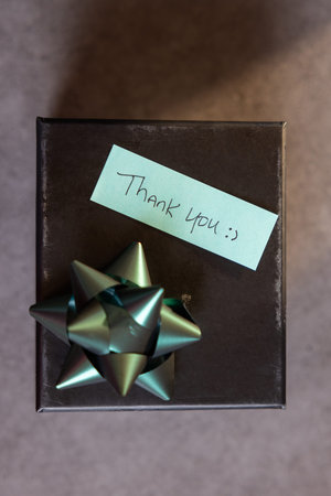 A box with a bow on top and a note that says Thank you written on it with a beam of light shining on the note.