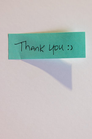 A blue sticky note with the words "thank you" written on it. The note is taped to a white wall or a surfaceの写真素材
