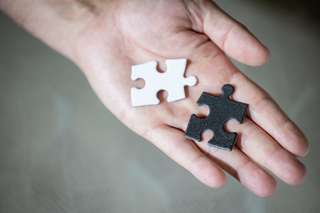 A hand holding two puzzle pieces, one white and one black both pieces have the same shape. The choice is a difficult concept.の写真素材