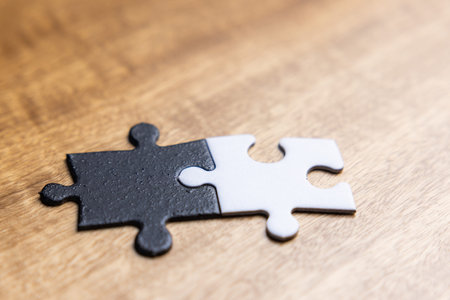 Two puzzle pieces with one black and one white on a wooden table. As a concept of unity between...