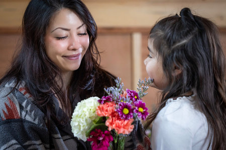 A woman is holding a bouquet of flowers and smiling at a her little girl. The girl is next to her mother. Concept of warmth and affection between mom and daughter ana Mother's Day.の写真素材