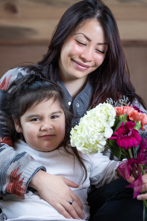 A woman is holding a bouquet of flowers and smiling at a her little girl. The girl is next to her...