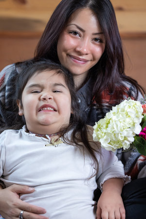 A woman is holding a bouquet of flowers and smiling at a her little girl. The girl is next to her mother. Concept of warmth and affection between mom and daughter ana Mother's Day.の写真素材
