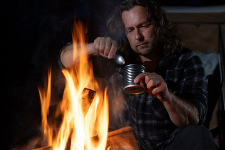 A man camping sitting by the fire eating canned food.の写真素材