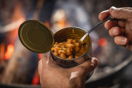 Hands holding a can of baked beans by the fire