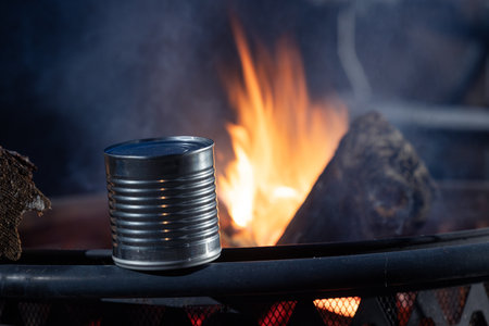 A can of food heating up next to a fire. The fire is raging and the can is silver.の写真素材