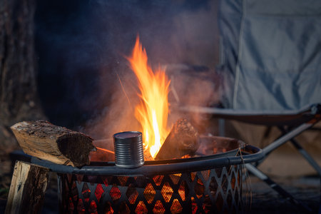 A can of food heating up next to a fire. The fire is raging and the can is silver.の写真素材