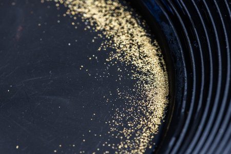 Closeup view of gold flakes collected in a black panning pan. Shiny metallic particles representing mining, prospecting, natural resources, and the search for wealth and treasure.の写真素材