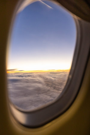 Sunrise view from a plane flying above the clouds framed by the window