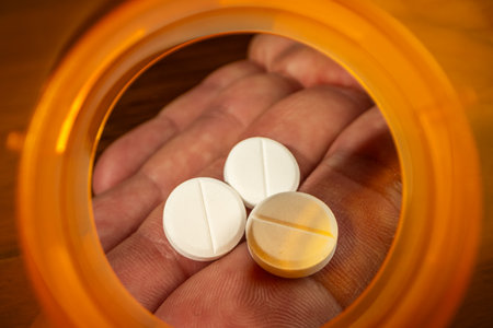 Dramatic macro view looking from the inside of an empty, bright orange prescription pill bottle. A human hand is visible reaching a small dose of tablets.の写真素材