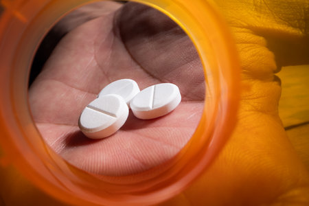 Dramatic macro view looking from the inside of an empty, bright orange prescription pill bottle. A human hand is visible reaching a small dose of tablets.の写真素材