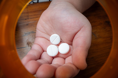 A powerful conceptual photograph showing a child's hand reaching for colorful, unattended prescription pills or medication.の写真素材