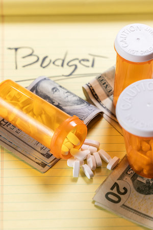 A visually impactful shot featuring prescription pill bottles and scattered US dollar bills (cash). This image symbolizes the high cost and financial burden of medication and the debt caused by healthcare expenses in the USA.の写真素材