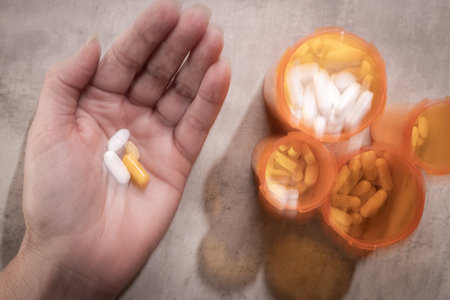 Substance abuse concept using intentional camera movement form a third-person view showing the hands of a person dispensing a daily dose of pills from a bottle.の写真素材