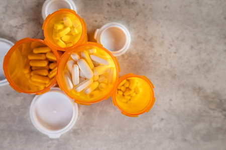 An overhead flat lay shot showing a mass or collection of pills and various open prescription bottles scattered on a surface.の写真素材