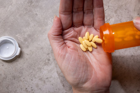 A third-person view showing the hands of a person dispensing a daily dose of pills from a bottle,...
