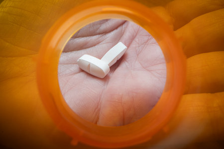 A powerful close-up, first-person view (POV) from inside an orange pill bottle as white pills are being dispensed into an adult hand.の写真素材