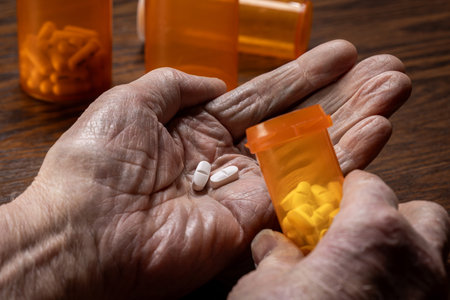 A detailed close-up shot of wrinkled, elderly senior hands carefully dosing pills from a prescription bottle.の写真素材