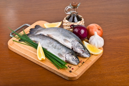 Fresh raw fish trout with peppers, onions and lemon on a wooden boardの写真素材