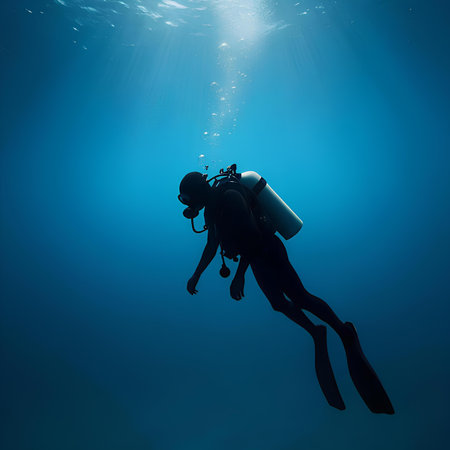 Silhouette of scuba diver standing in deep blue water.の素材