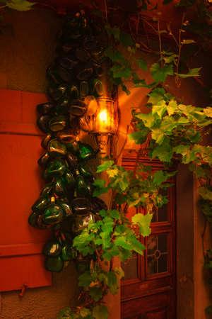 Porch of abandoned building overgrown with grapevine and fresh green leaves with hanging ripe grape bunches. Old brown wooden door and stone stairs of dilapidated house in European cityの写真素材