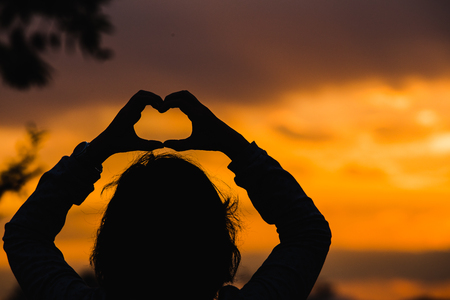Women Silhouette with Hands in Heart Shape on Sunset Backgroundの写真素材